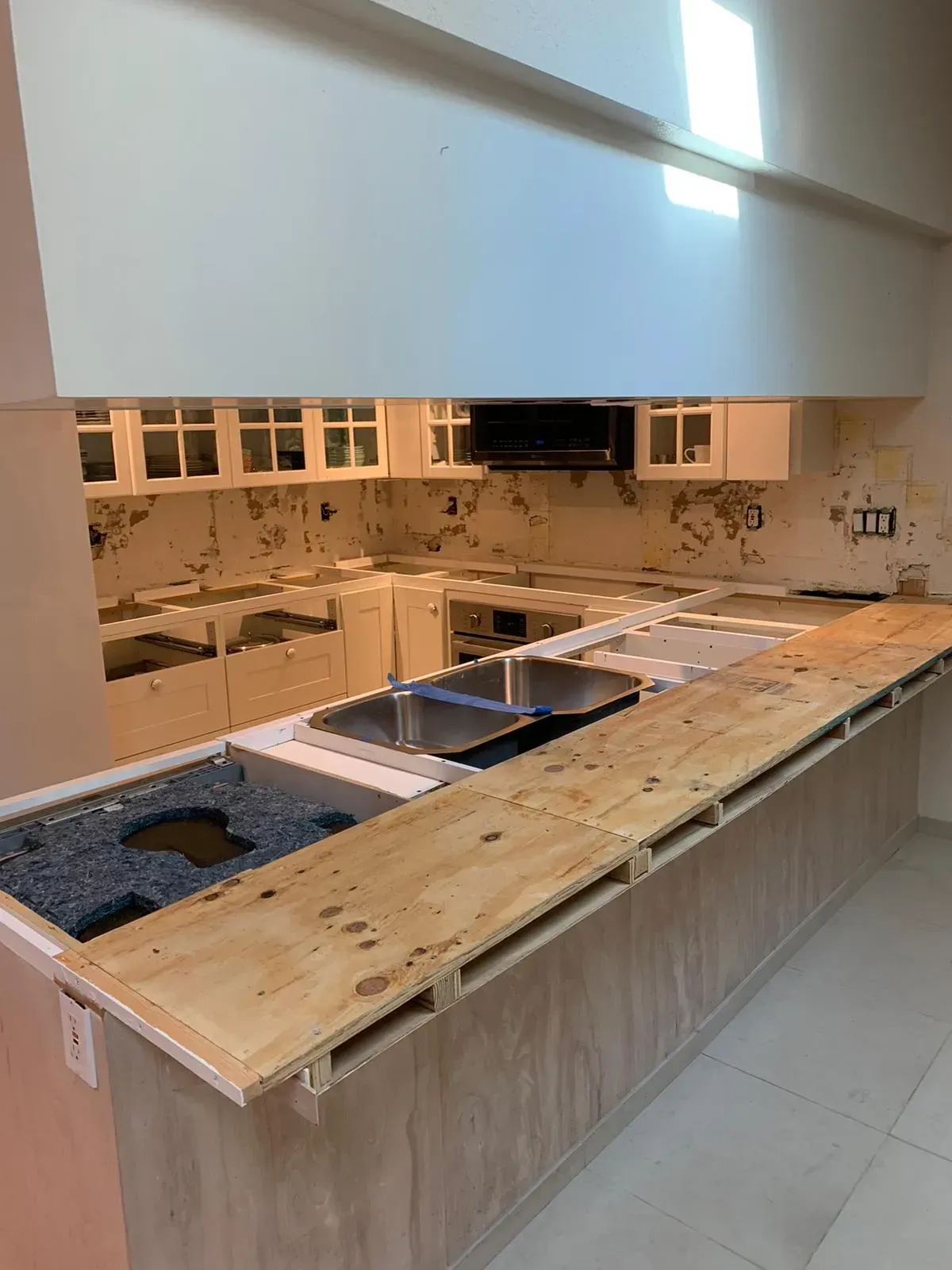 Unfinished kitchen with long island, sink cutouts, plywood countertop, and tiled backsplash under construction