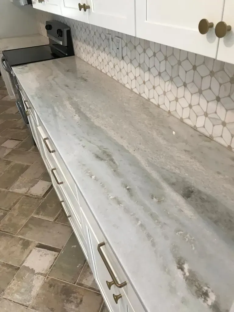 Empty kitchen countertop with light gray stone surface, white cabinets, and hexagon tile backsplash