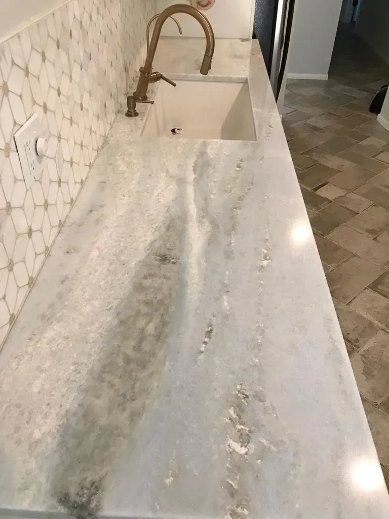 White marble kitchen countertop with sink, brass faucet, and tiled backsplash under soft light