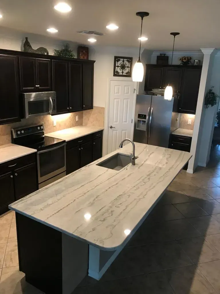 Modern kitchen with dark cabinets, stainless appliances, and a large white island under pendant lights