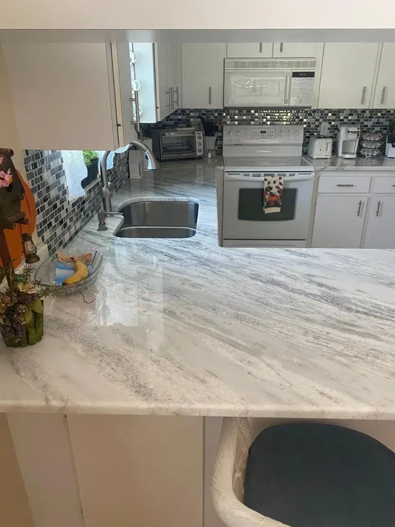 Modern kitchen with marble island, stainless stove and sink, and a dark chair at the counter.