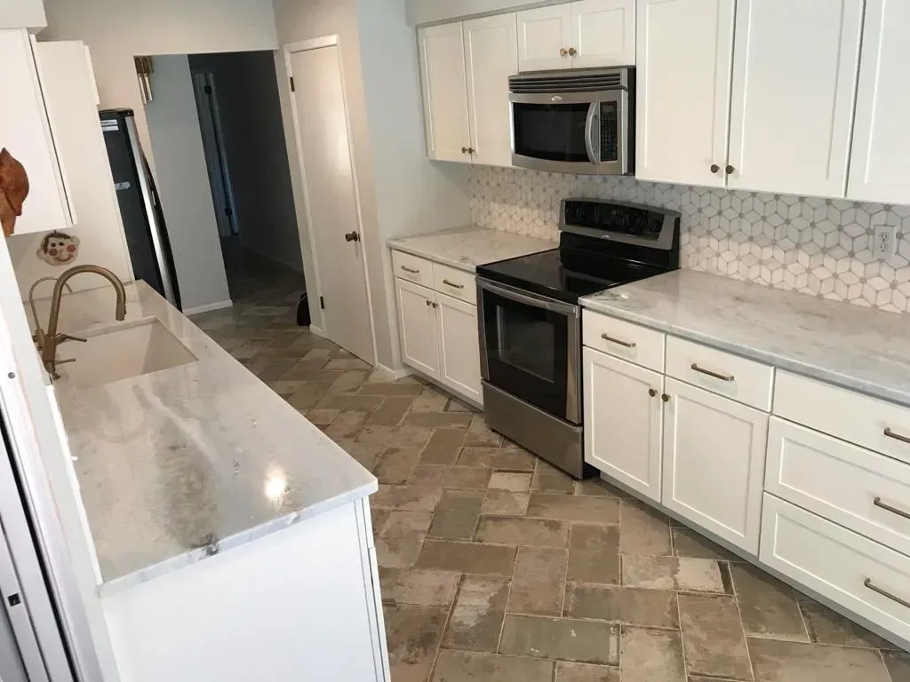 Bright white galley kitchen with black stove, stainless microwave, and tiled floor