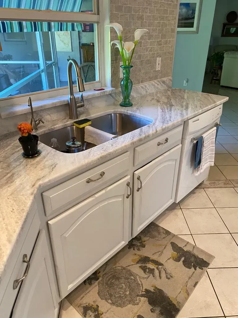 White kitchen sink and granite countertop with flowers and tiled floor rug.