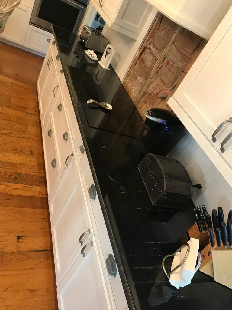 Kitchen counter with black countertop, white cabinets, toaster, coffee maker, and utensils by a window.