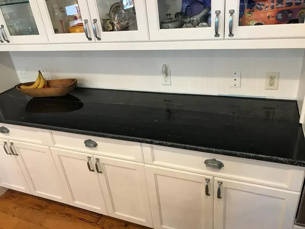 White kitchen counter with black granite top, cabinets below, and a bowl of bananas on the left.
