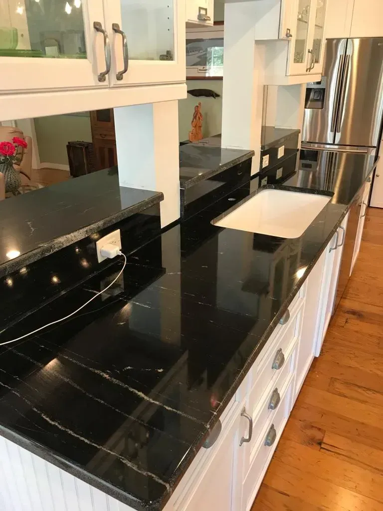 Kitchen with glossy black countertop, white cabinets, stainless refrigerator, and hardwood floor