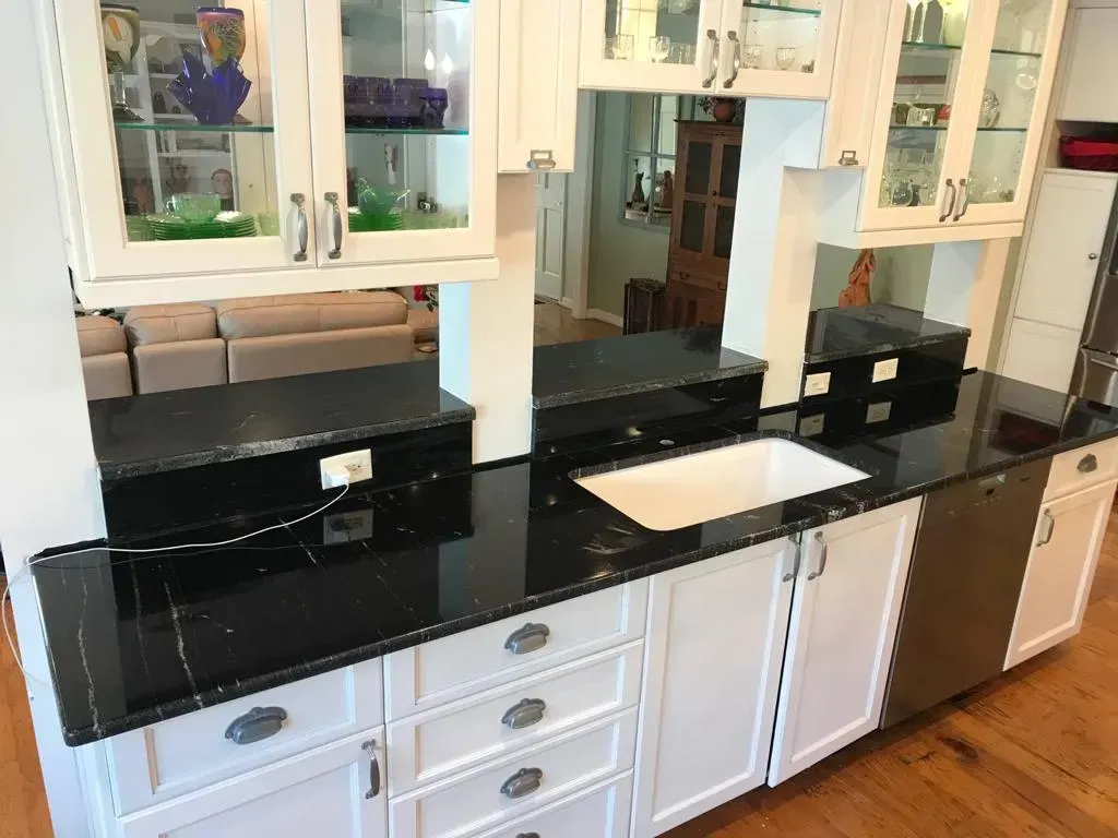Kitchen vanity with black countertops, white cabinets, and two sinks beneath mirrored cabinets.
