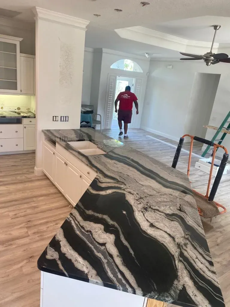 Kitchen with broken island cabinet and exposed contents; worker in red stands in a bright open-plan home.