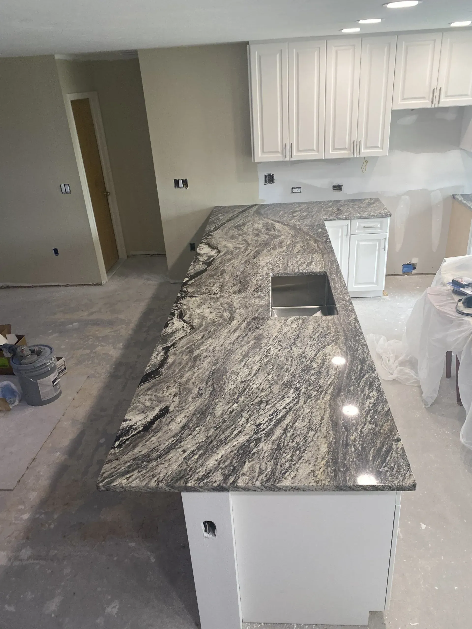 Kitchen with granite island countertop, white cabinets, and carpeted living area in the background.
