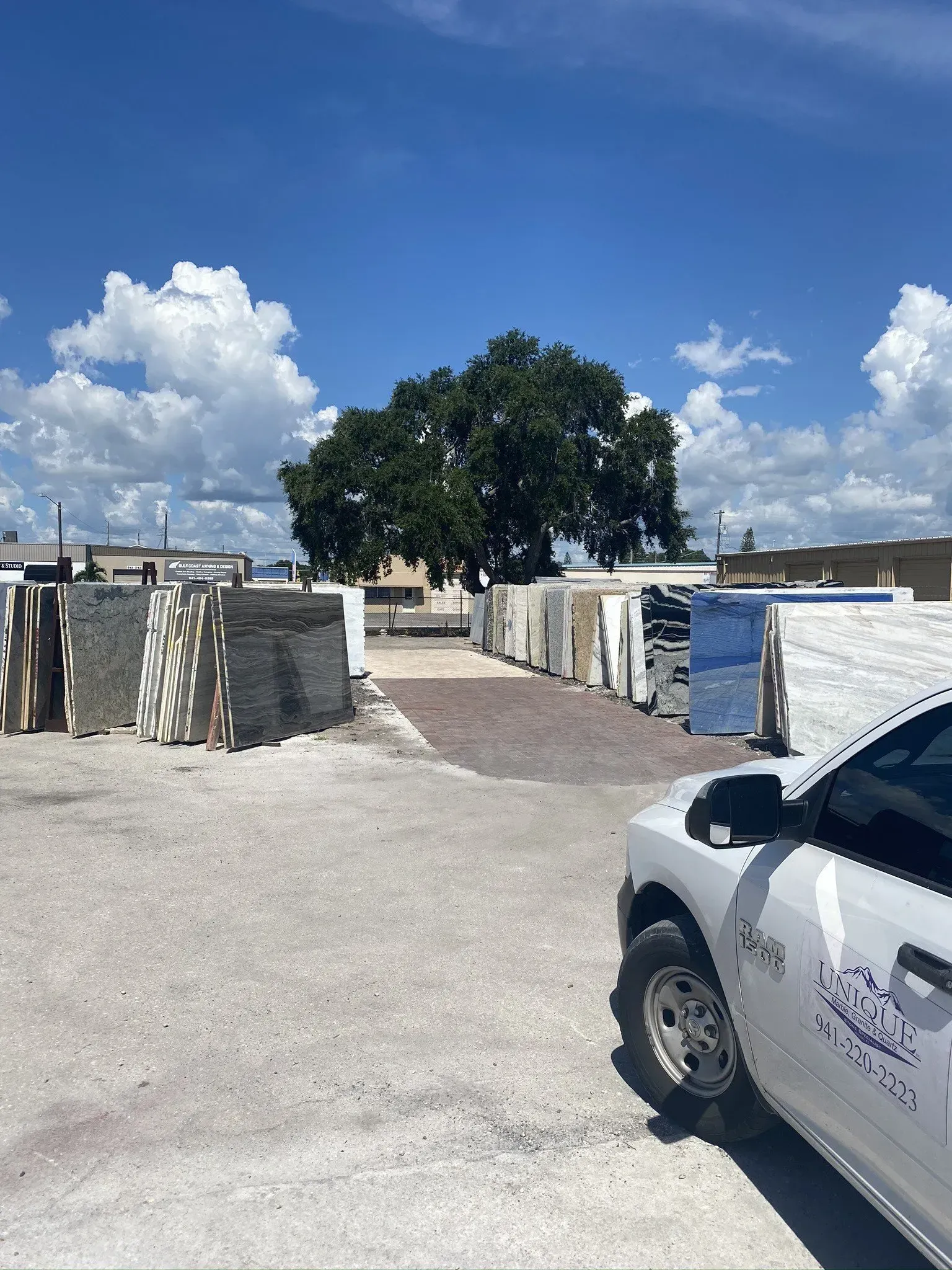 Gravel lot with rows of corrugated metal stalls and a white truck under a bright blue sky with clouds