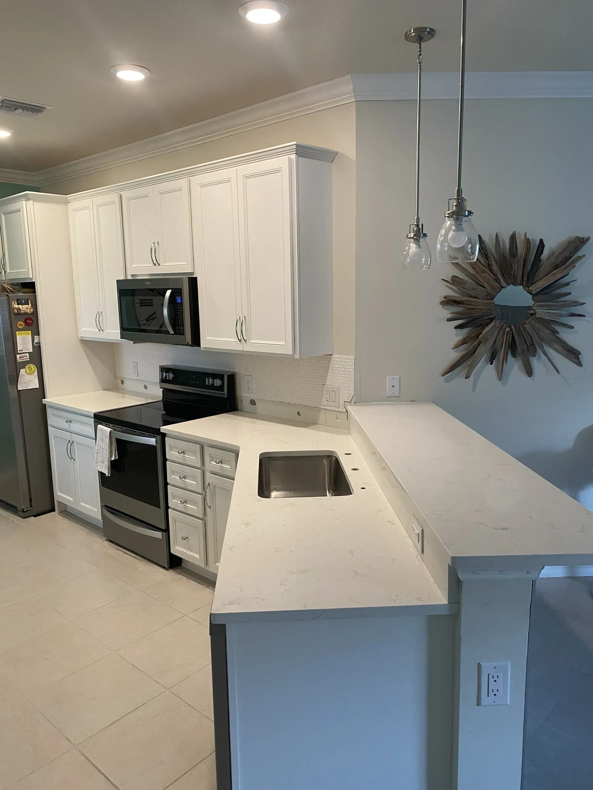Bright white kitchen with stainless appliances, tiled floor, and a starburst wall decor.
