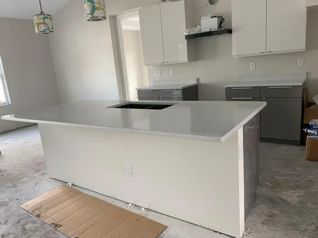 Bright kitchen with white cabinets, gray countertops, and a central island on cardboard flooring.