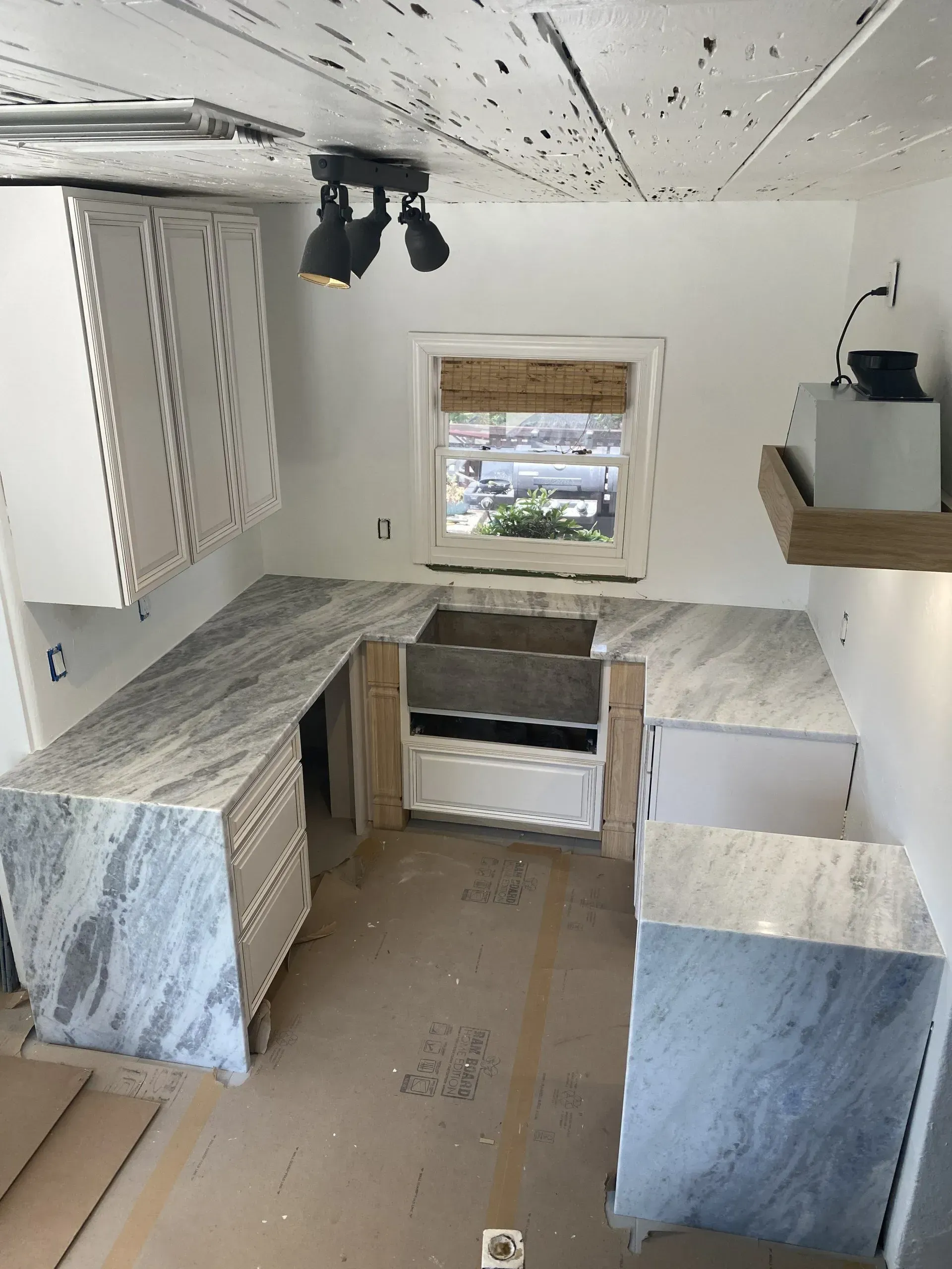 Unfinished kitchen with marble-look cabinets, white ceiling, and a window above the sink.