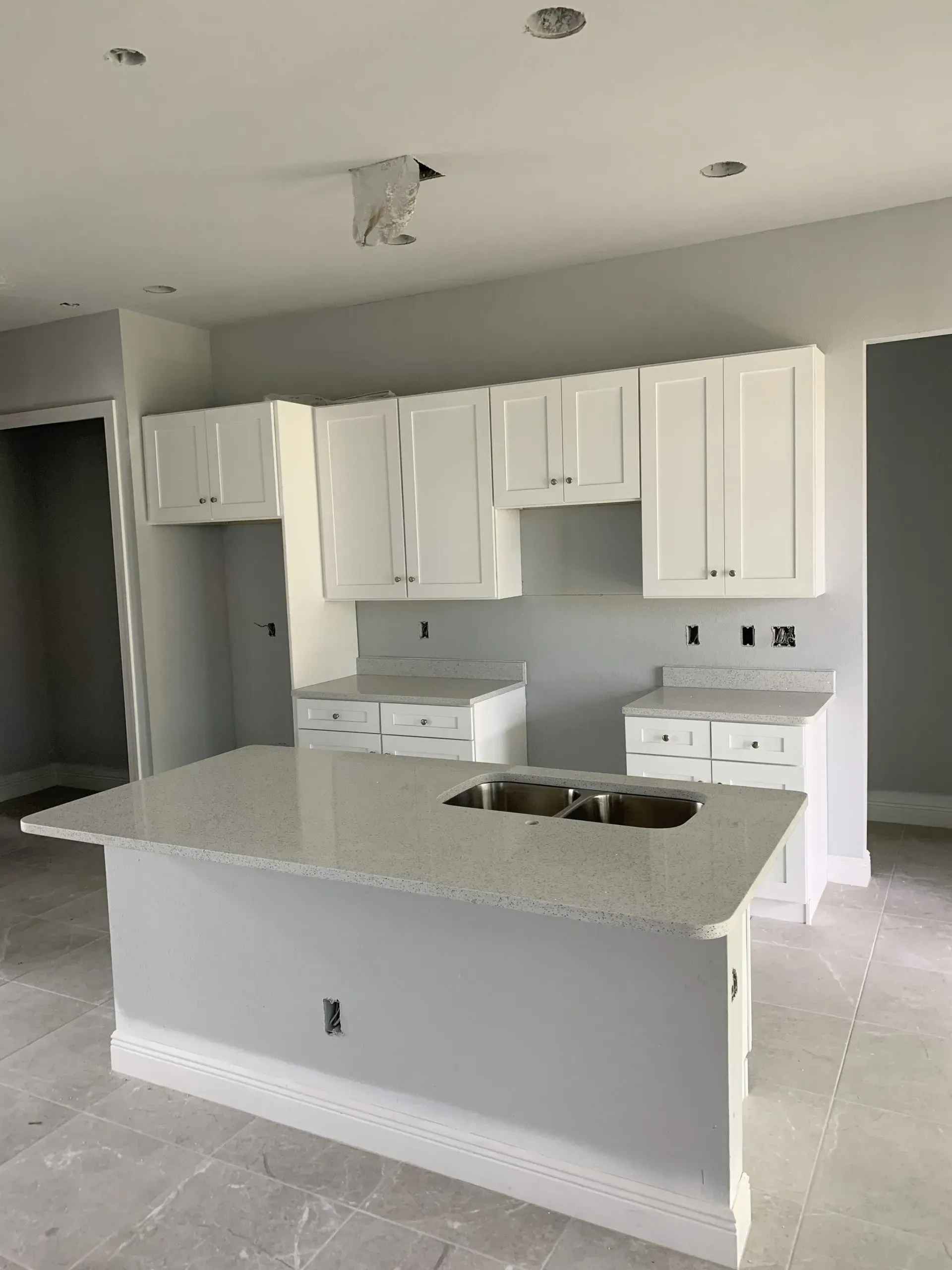 Bright white kitchen with island, cabinets, and recessed ceiling lights in an empty home.
