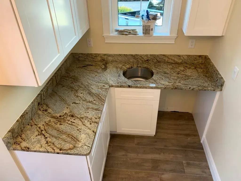 L-shaped kitchen countertop with granite-look surface, white cabinets, and a sink beneath a window.