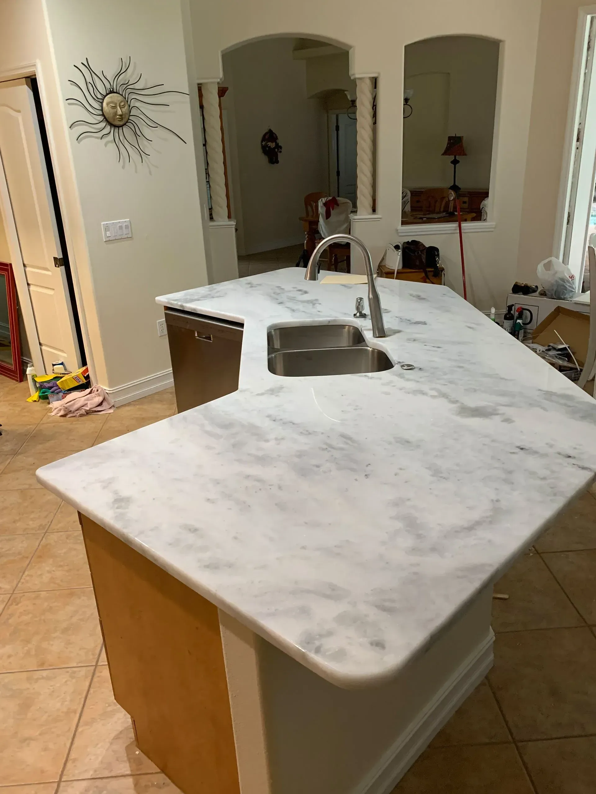 Kitchen island with marble countertop and stainless sink in a tiled home interior