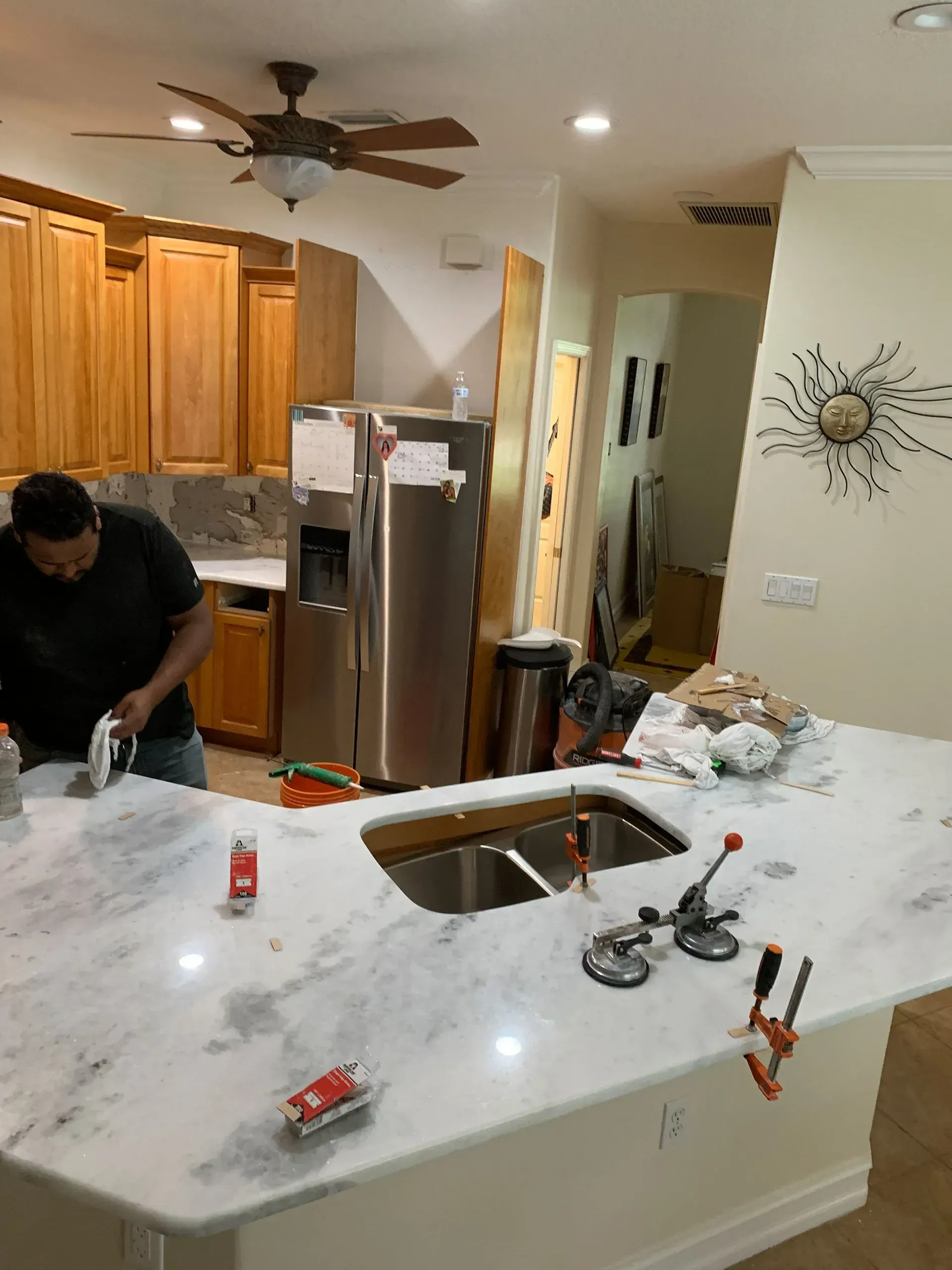 Kitchen under renovation with marble countertop, tools, and a worker installing a sink