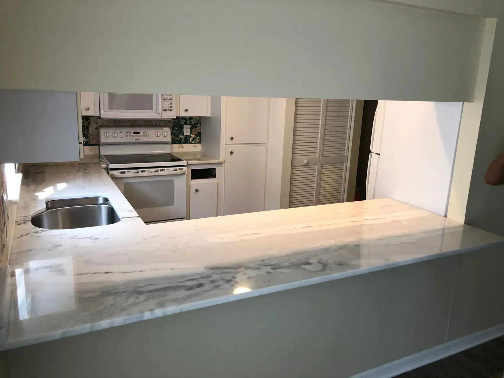 Kitchen viewed through pass-through window, with white stove, sink, and marble countertop.