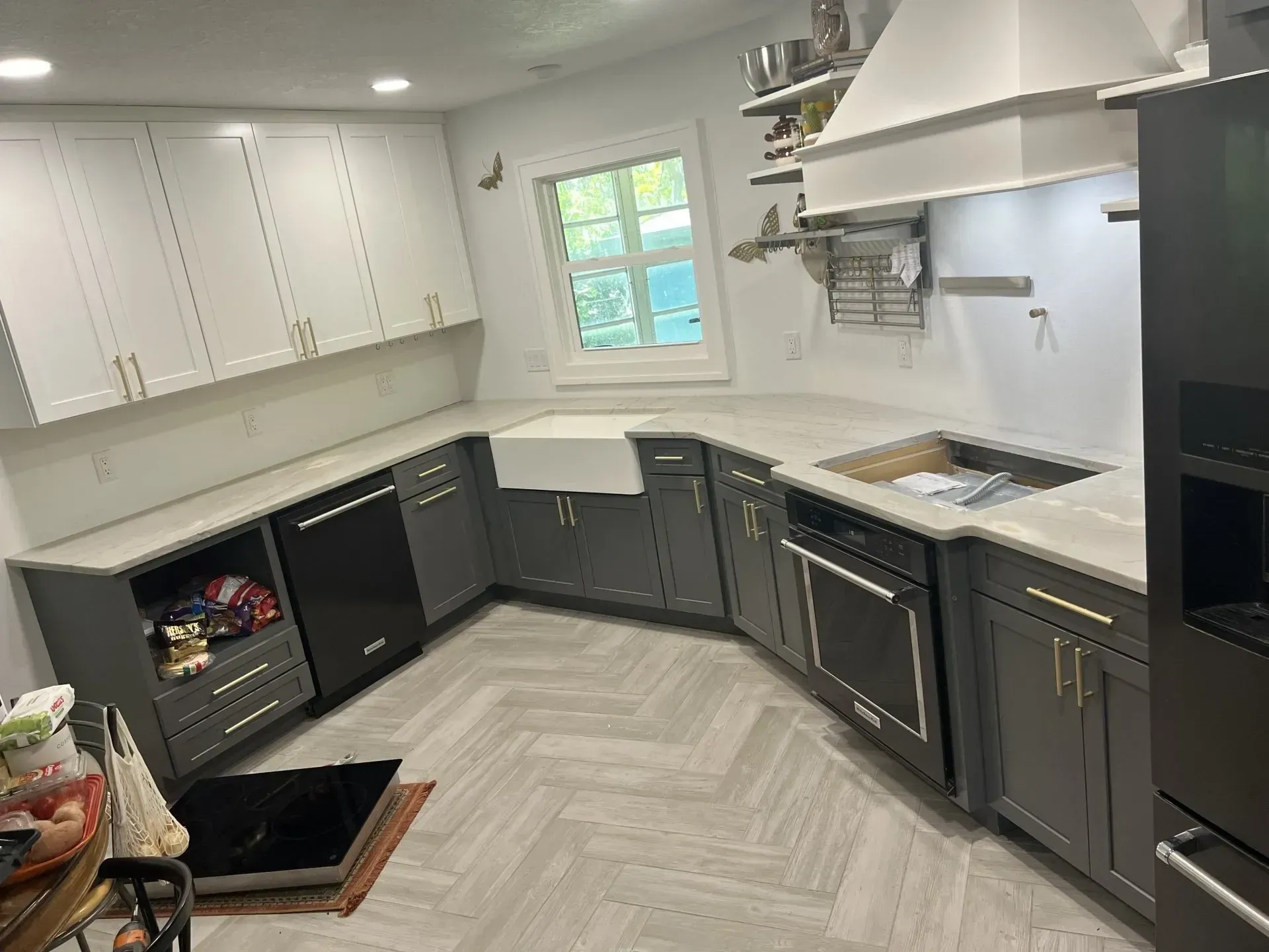 Bright modern kitchen with white cabinets, dark lower cabinets, herringbone floor, and a window over the sink