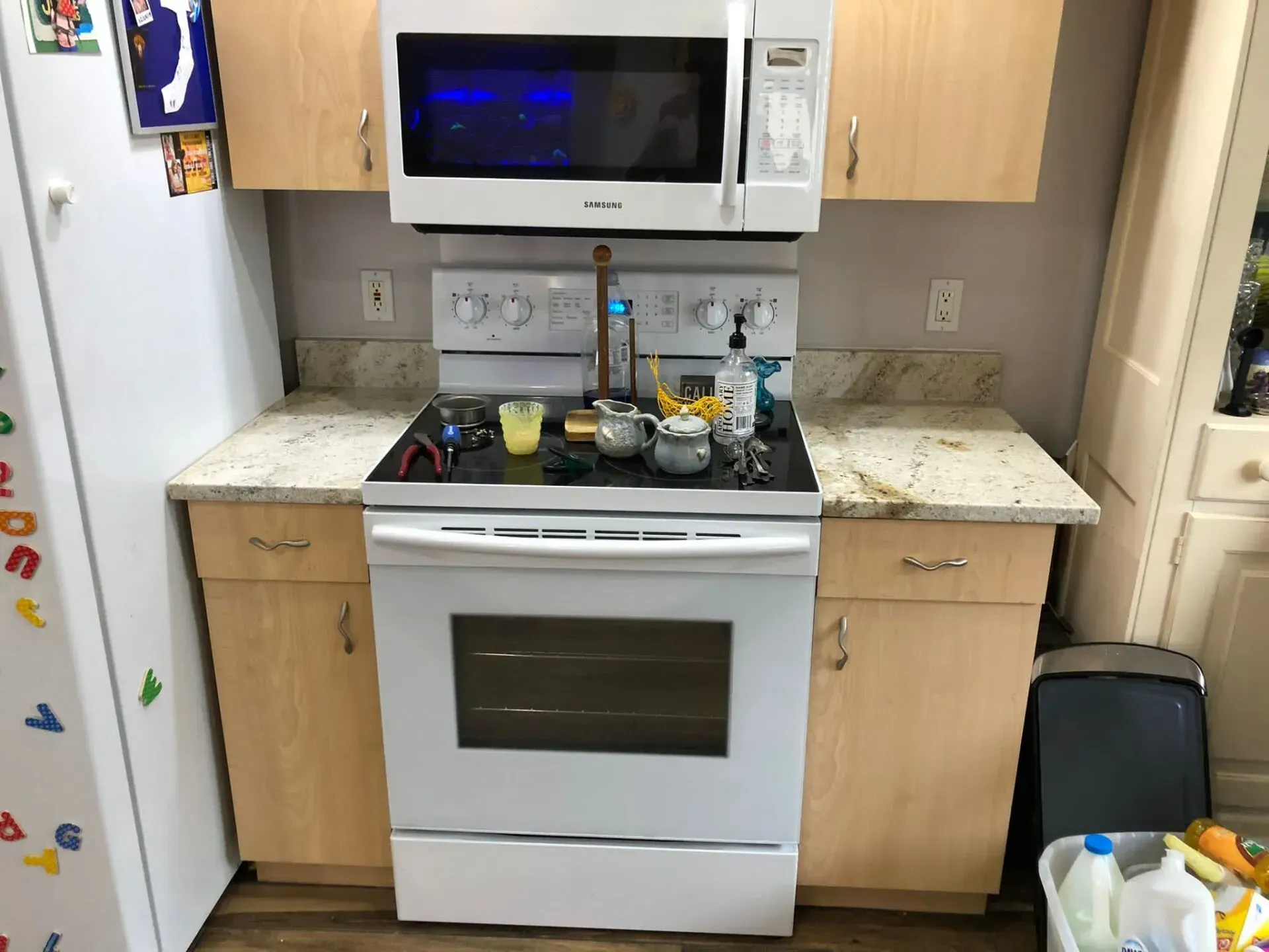Small kitchen with white stove, microwave, and granite countertops cluttered with dishes.