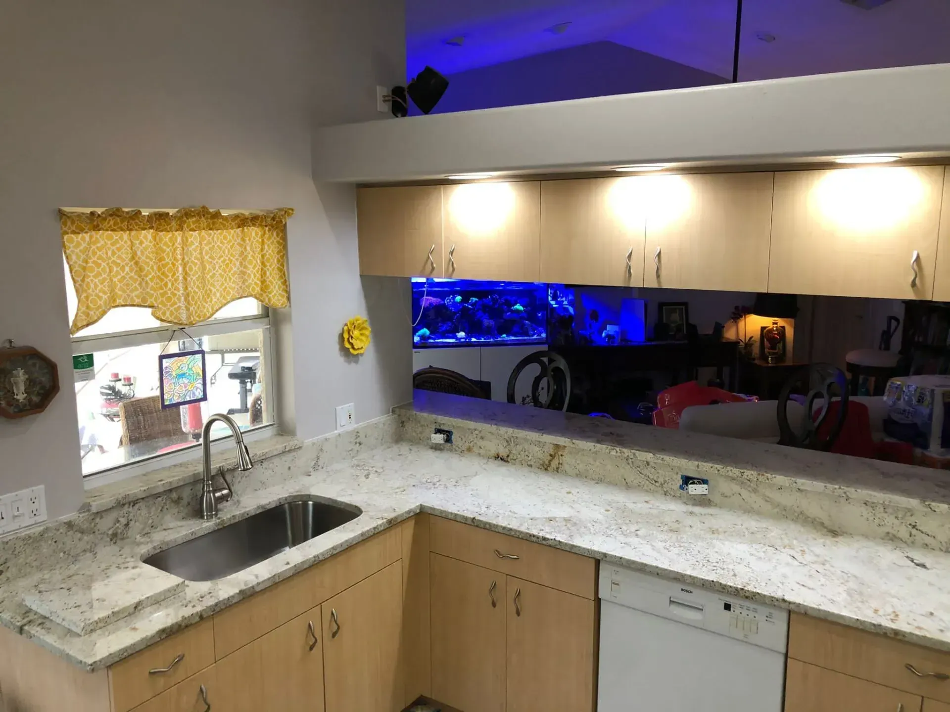 Modern kitchen with granite counters, sink by window, wood cabinets, and blue-lit glass backsplash display