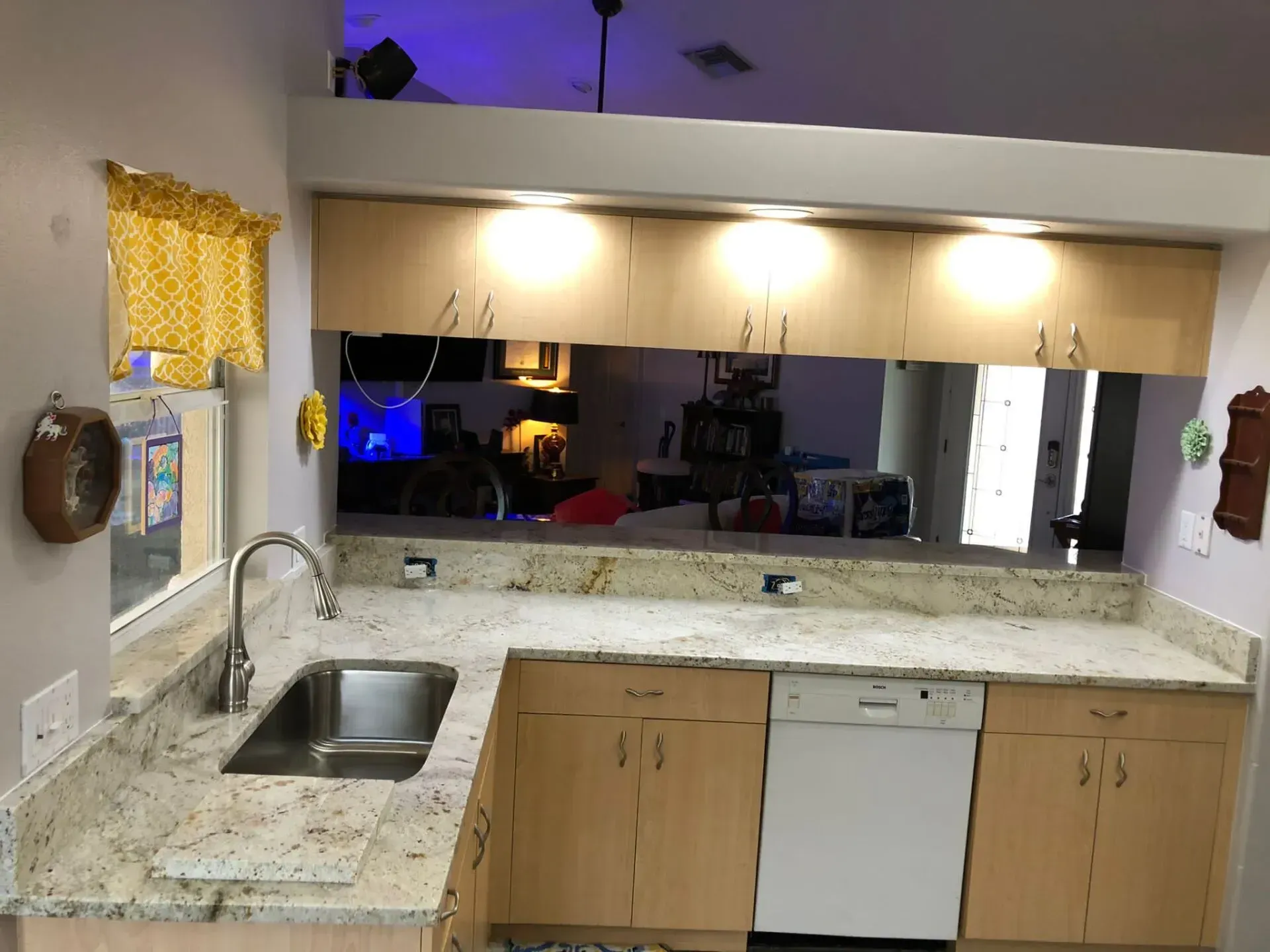 Kitchen with granite countertops, sink, dishwasher, and large pass-through mirror under warm lighting.