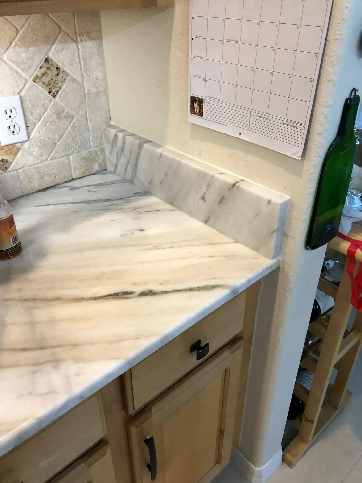 Marble kitchen countertop with tiled backsplash, white cabinets, and a green bottle on the right.