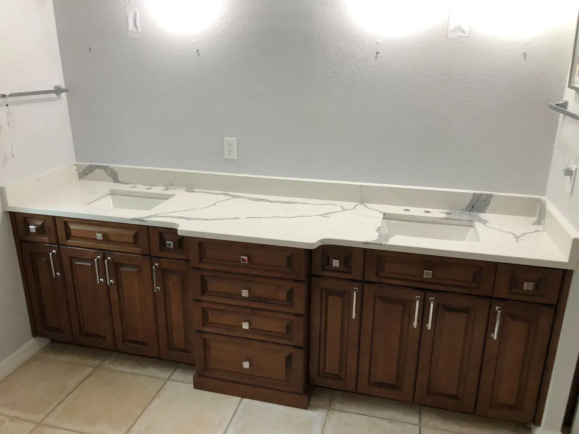 Bathroom vanity with dark wood cabinets and a white countertop against a light gray wall.