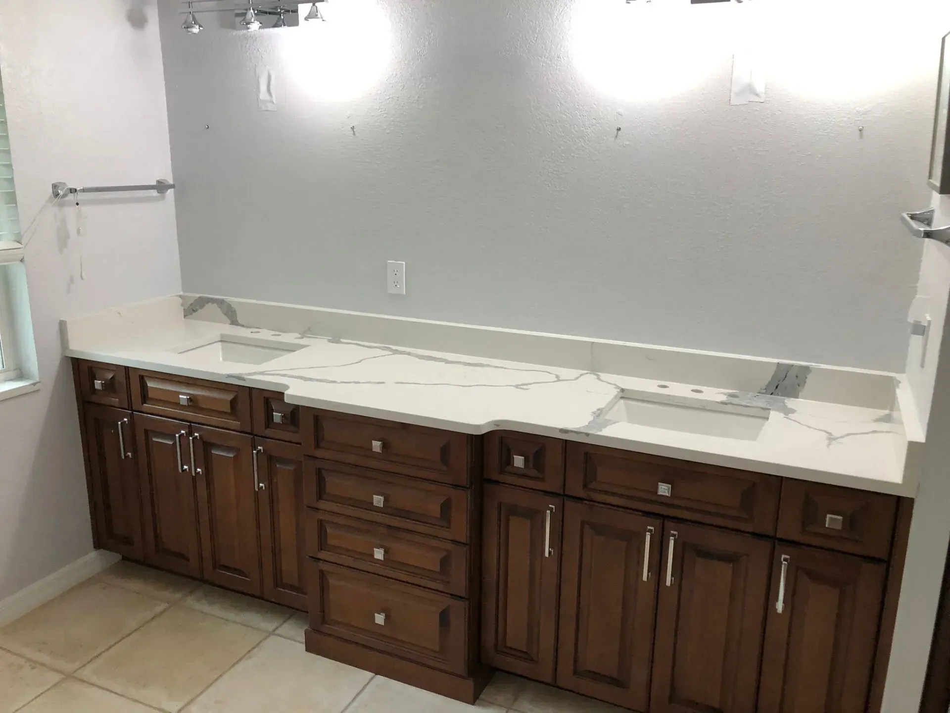 Bathroom vanity with dark wood cabinets, white countertop, and two wall lights above a mirror.