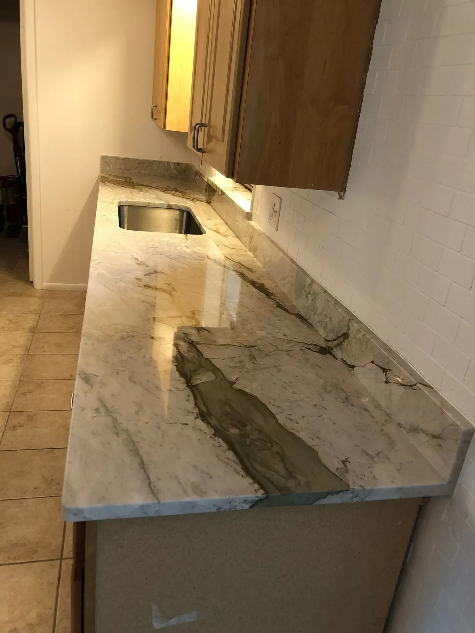 Damaged bathroom countertop with cracked marble sink area and debris, beside a wooden cabinet.