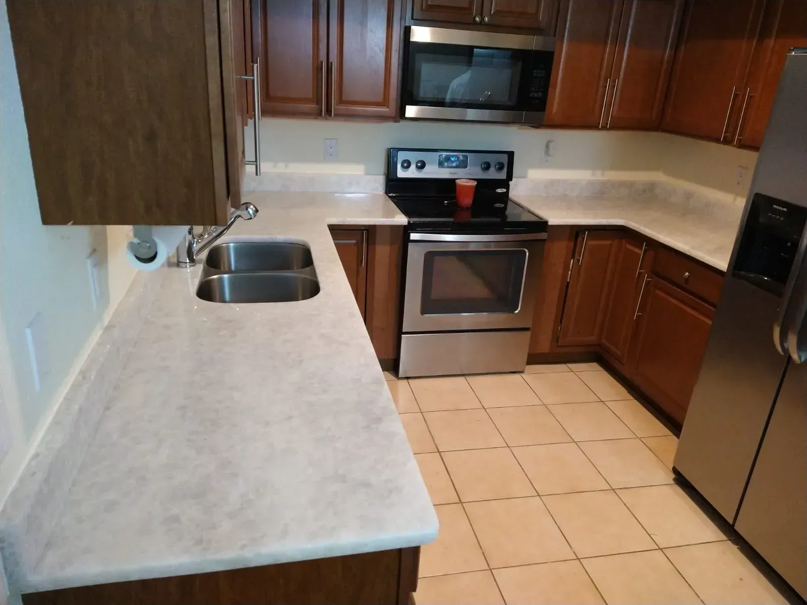 Small kitchen with wood cabinets, light countertops, tile floor, stainless stove, sink, and refrigerator.