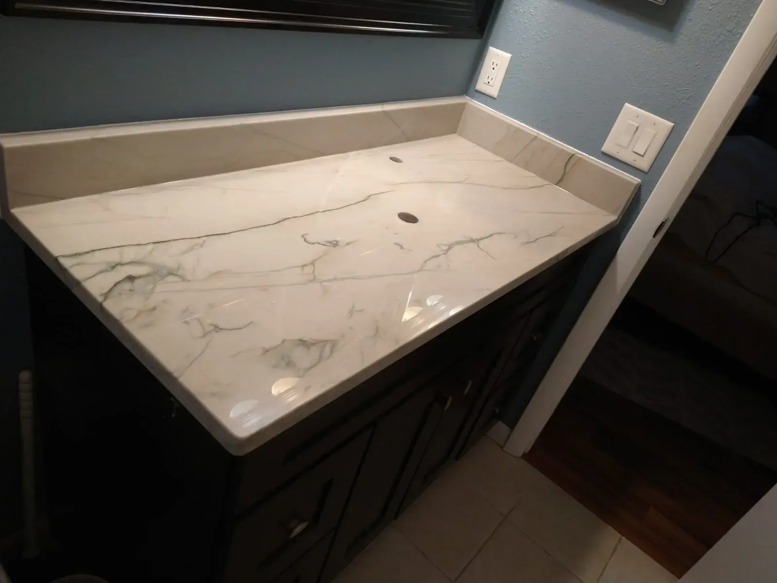 White marble bathroom countertop with dark cabinets and mirror in a small vanity area