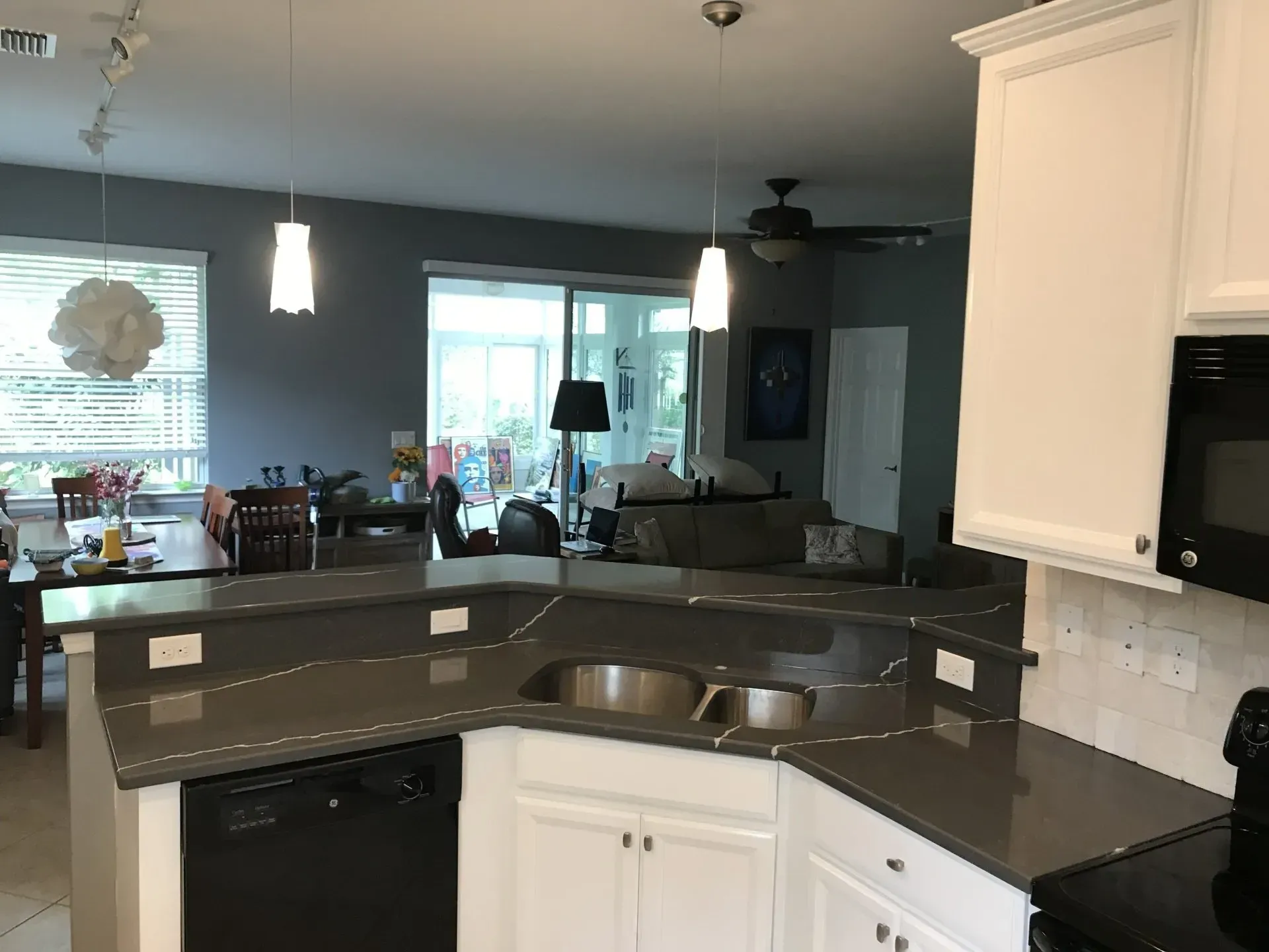 Modern kitchen with gray countertops, white cabinets, and a view into a living room with large windows.