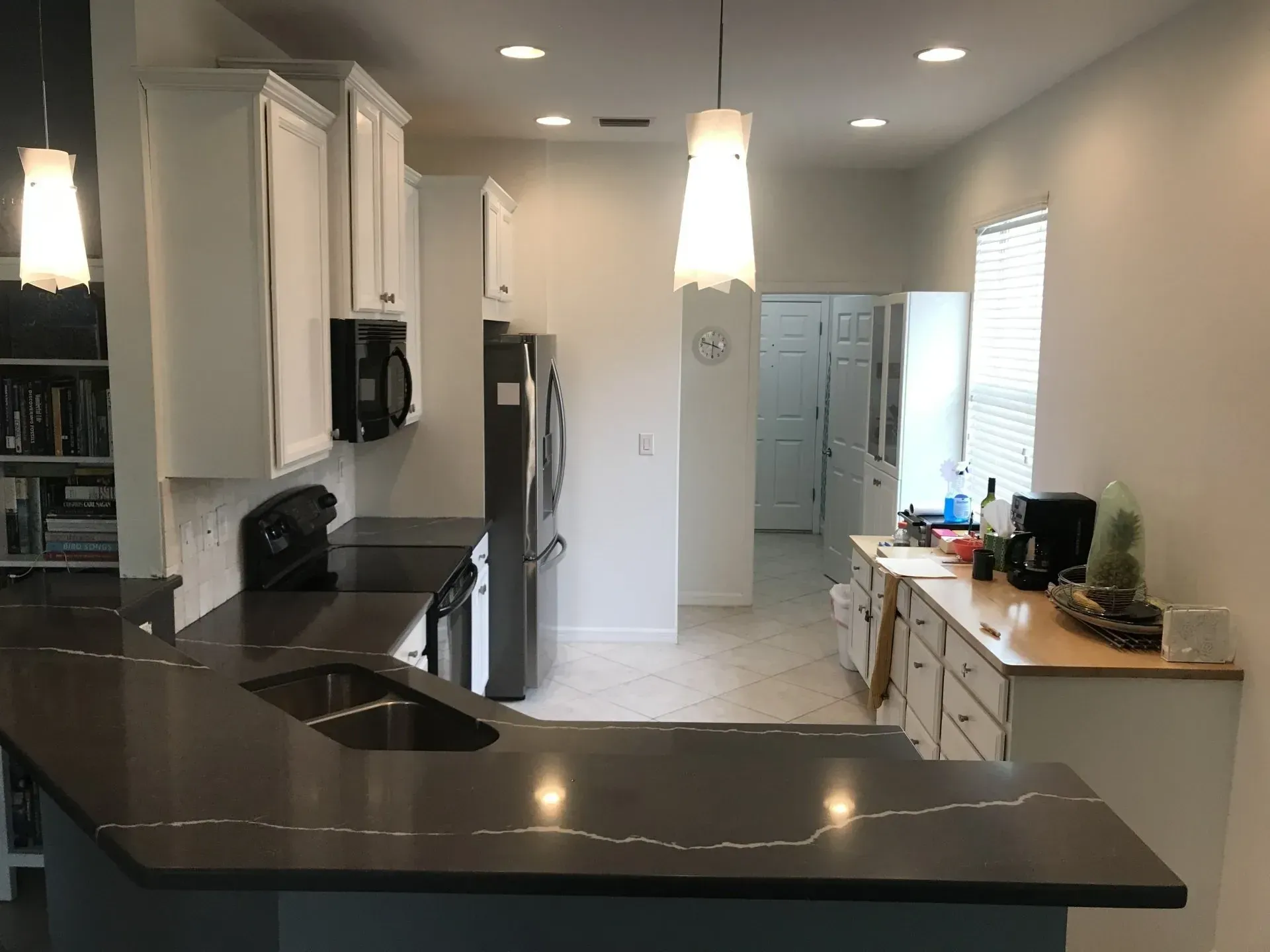 Modern kitchen with dark countertops, white cabinets, and stainless steel appliances, viewed from the island.