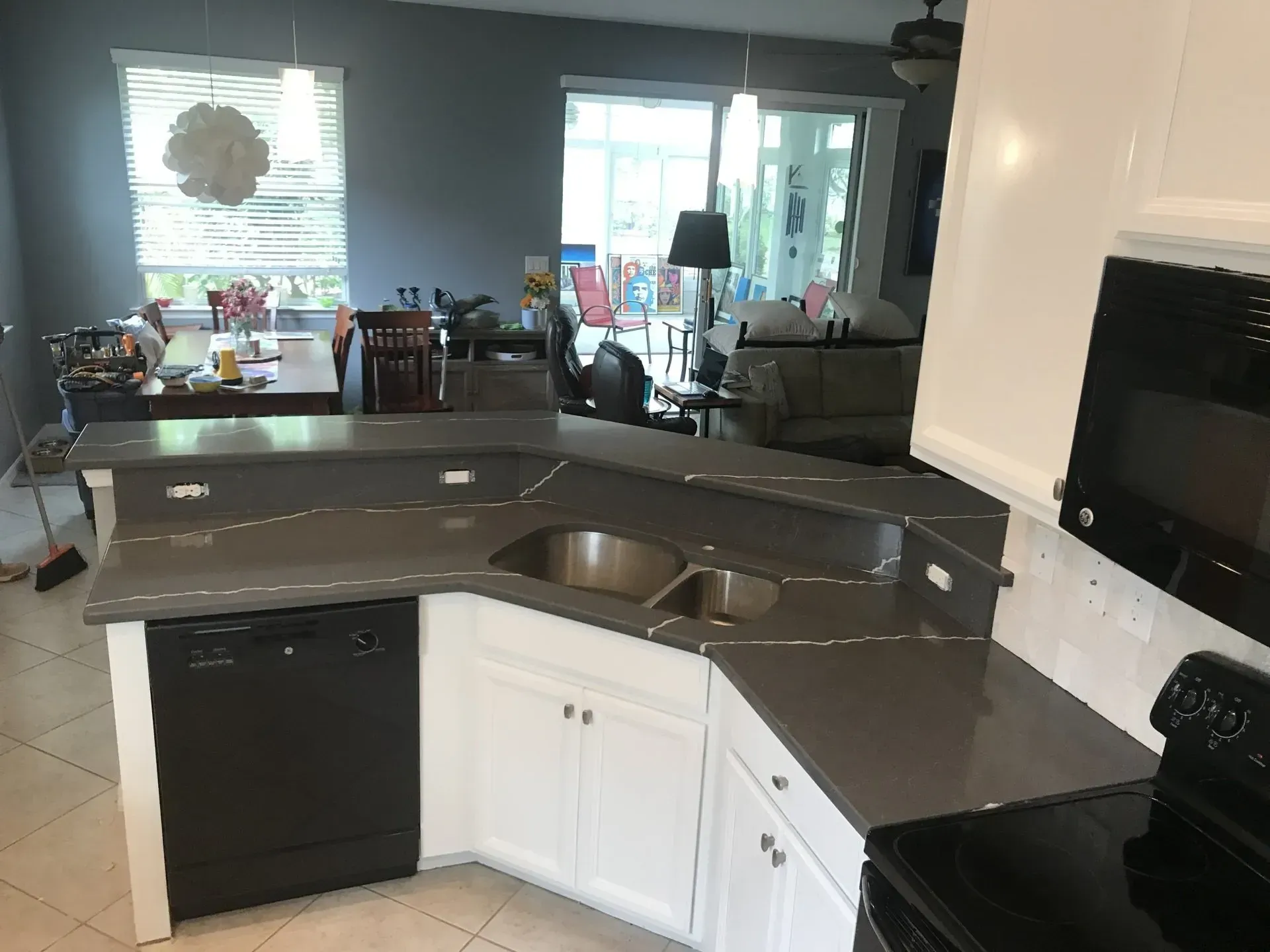 Modern kitchen with curved granite island, black and white cabinets, and a view into a sunlit dining area