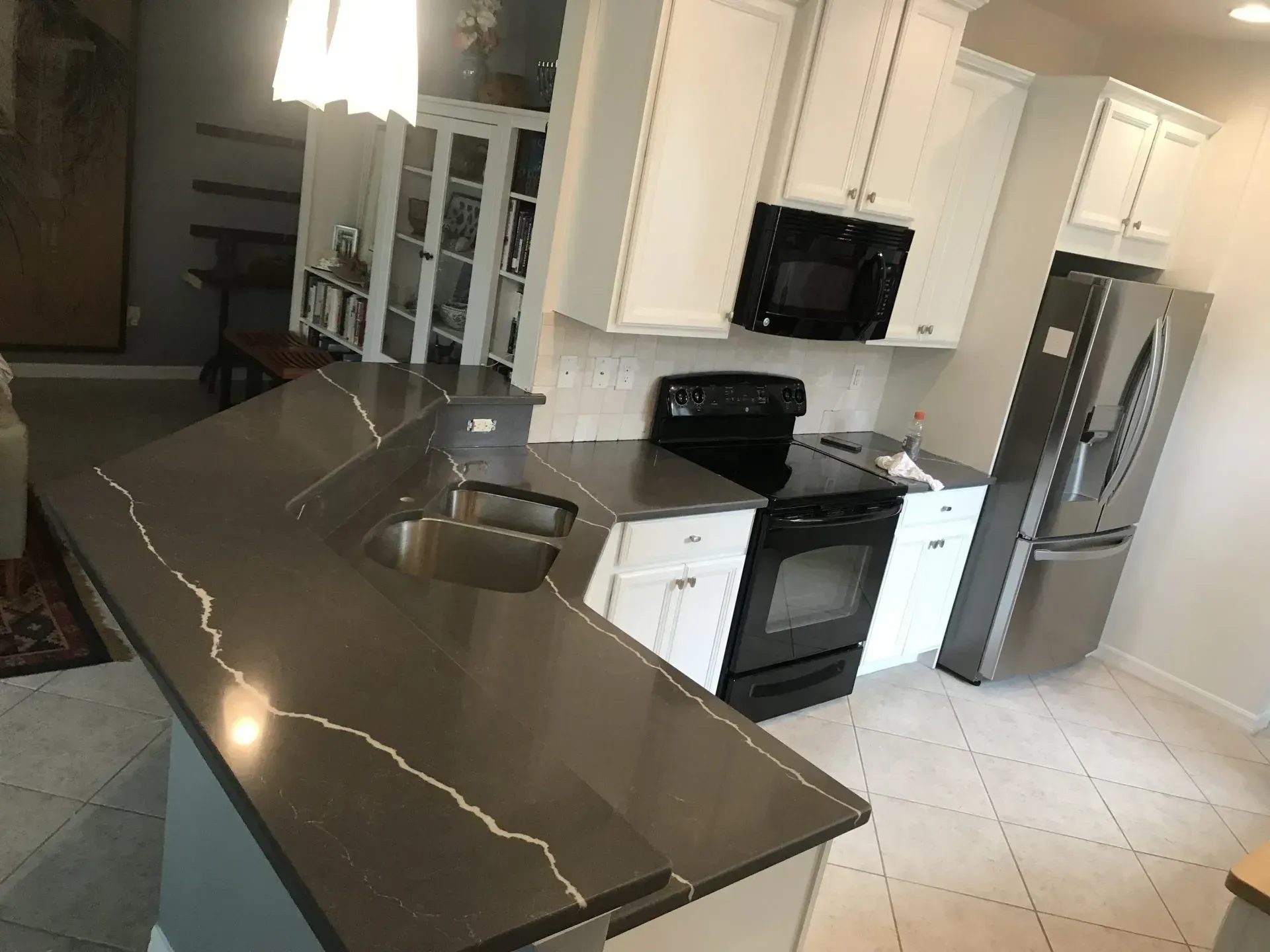 Modern kitchen with dark granite island, white cabinets, stainless steel appliances, and tile floor