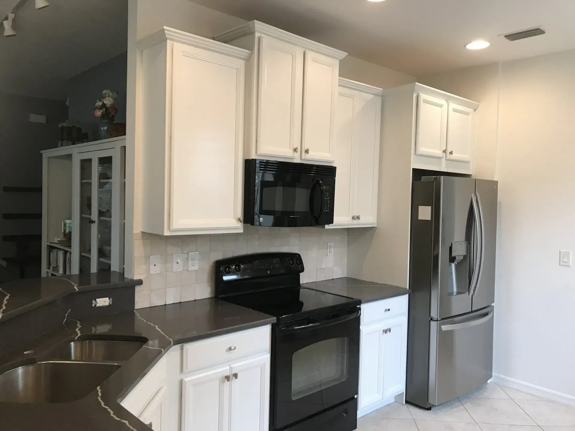 Modern kitchen with white cabinets, black countertops, stainless fridge, and black stove.