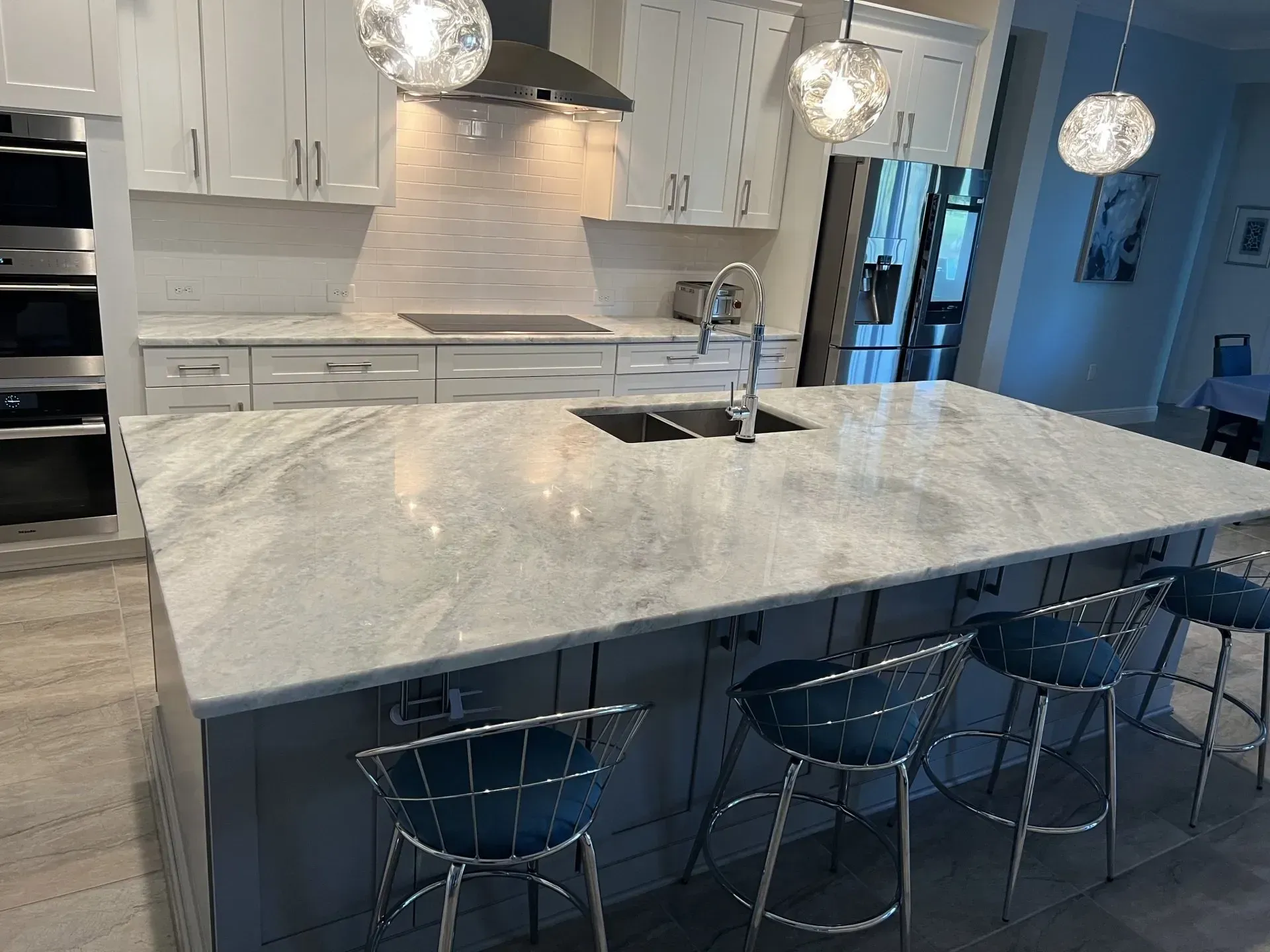 Modern kitchen with marble island, white cabinets, pendant lights, and three barstools