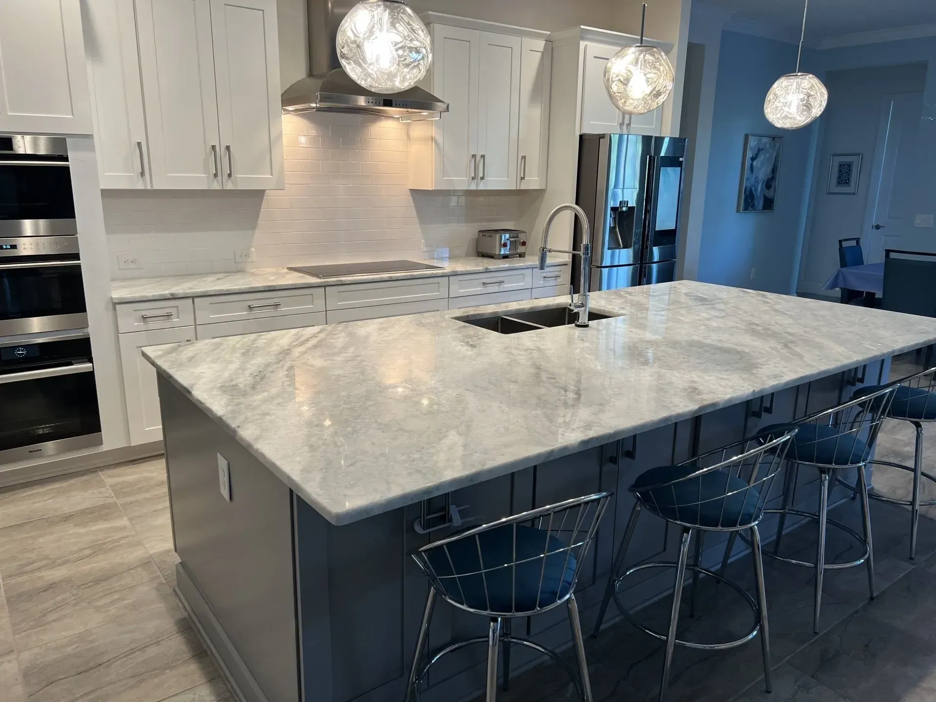 Modern kitchen with white cabinets, marble island, pendant lights, and blue barstools