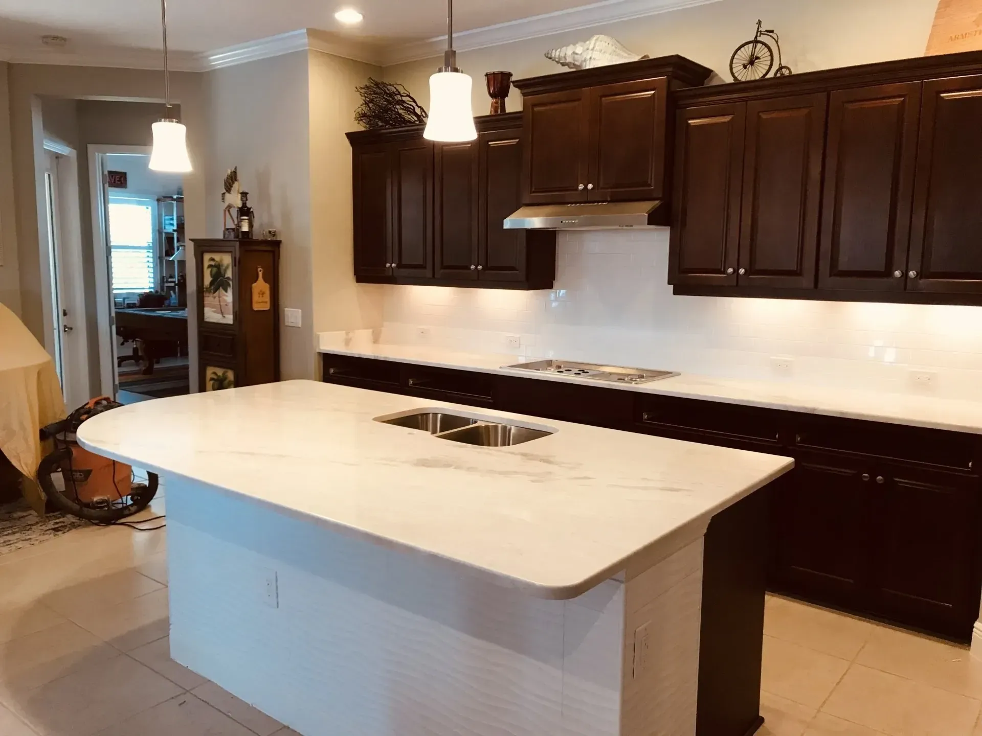 Modern kitchen with dark wood cabinets, white island countertop, and pendant lighting.