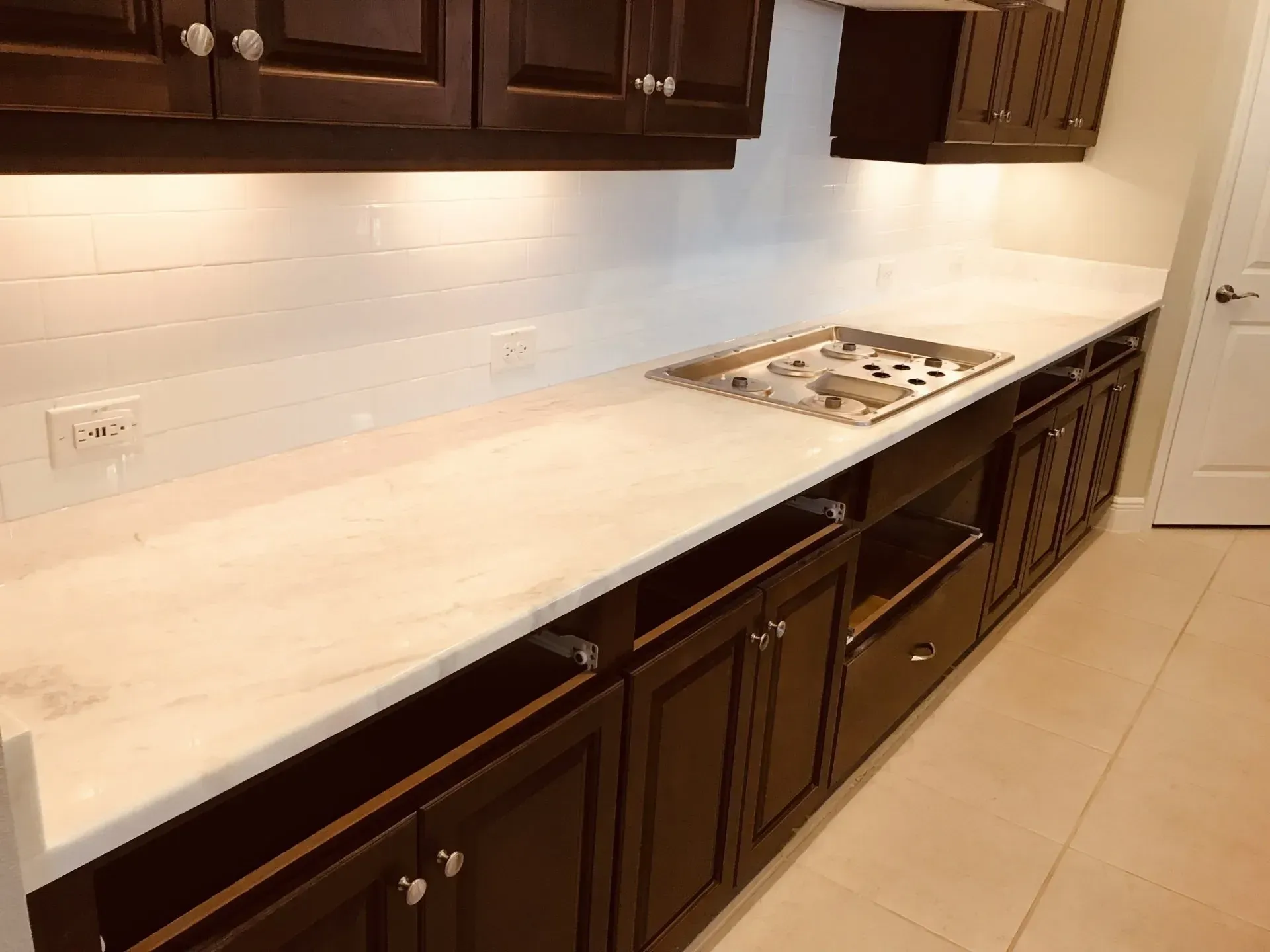 Modern kitchen with white countertops, dark wood cabinets, and a built-in cooktop along the wall