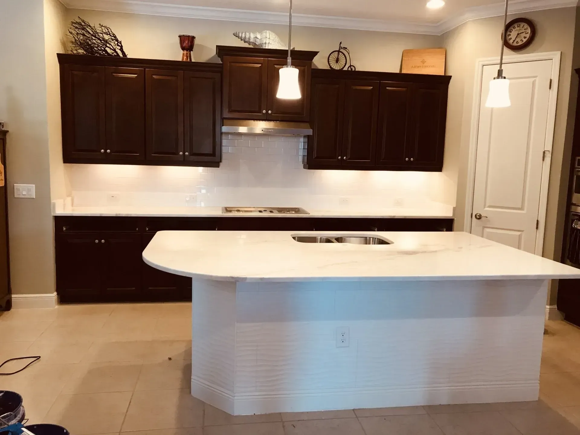 Modern kitchen with dark cabinets, white island, tile floor, and pendant light