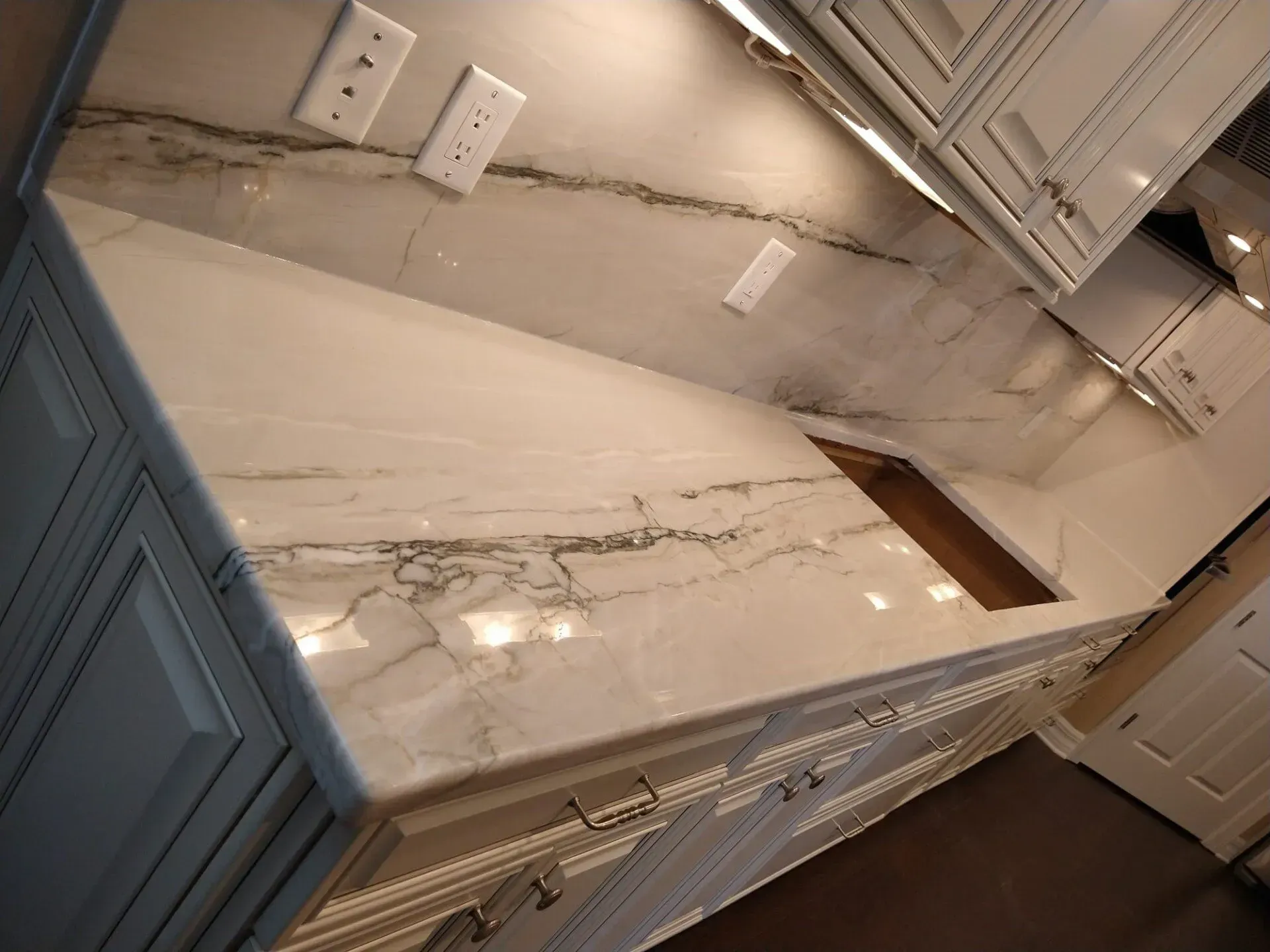 Kitchen with white marble countertop, blue cabinets, and wall outlets under upper cabinets.
