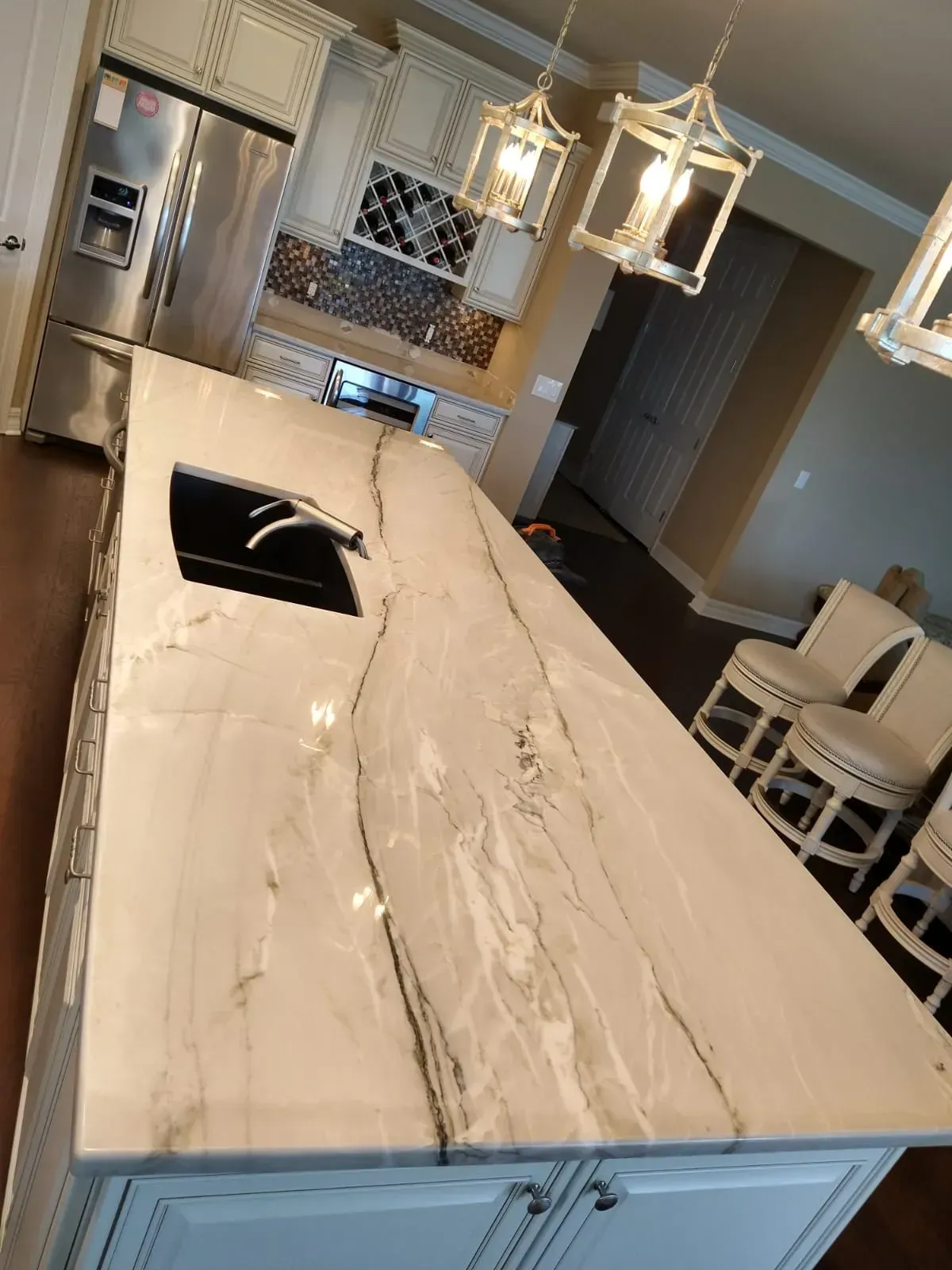 Modern kitchen with marble island, stainless fridge, pendant lights, and stools