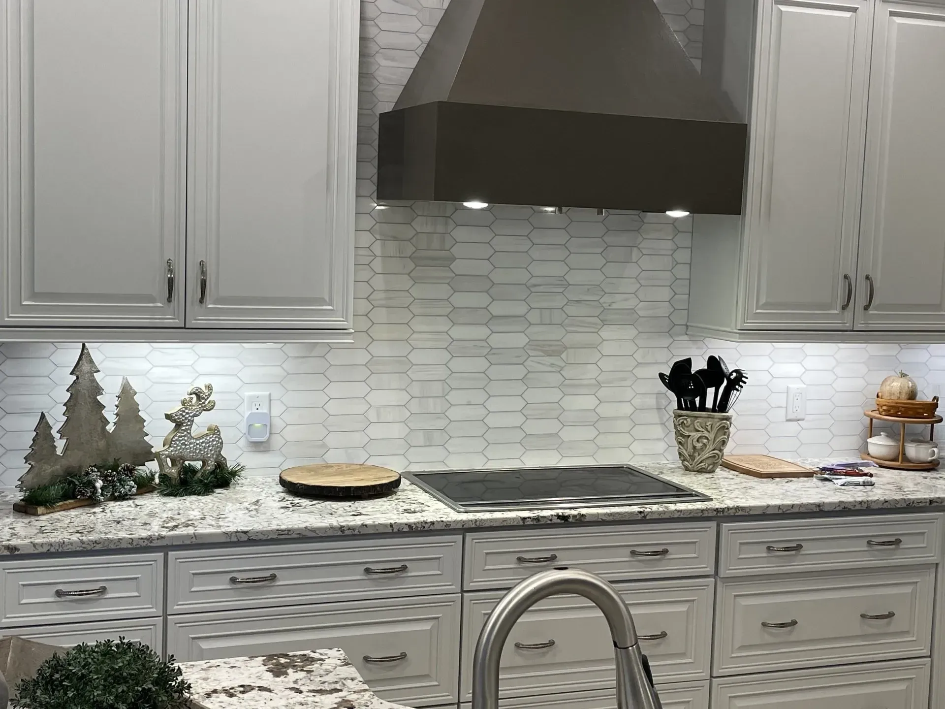 Modern white kitchen with marble backsplash, black range hood, stove, and countertop decor