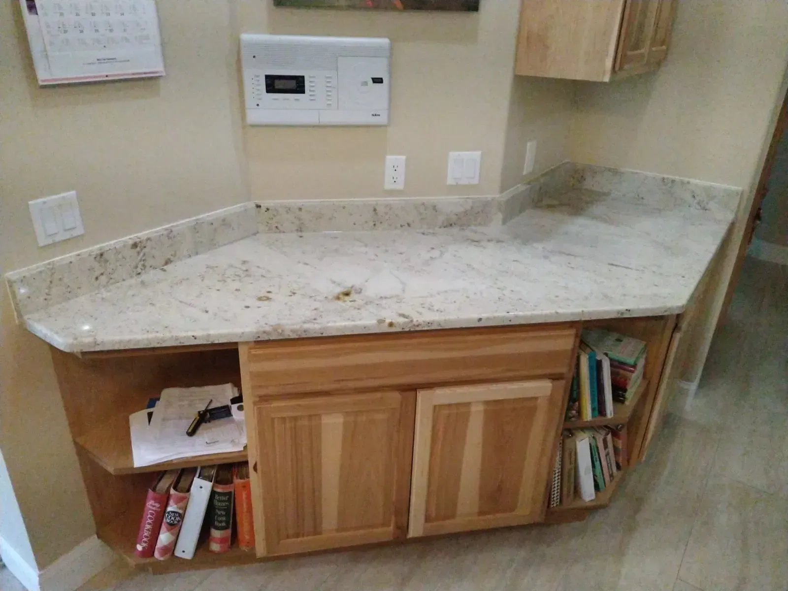 Kitchen countertop with beige granite, light wood cabinets, and a built-in wall control panel
