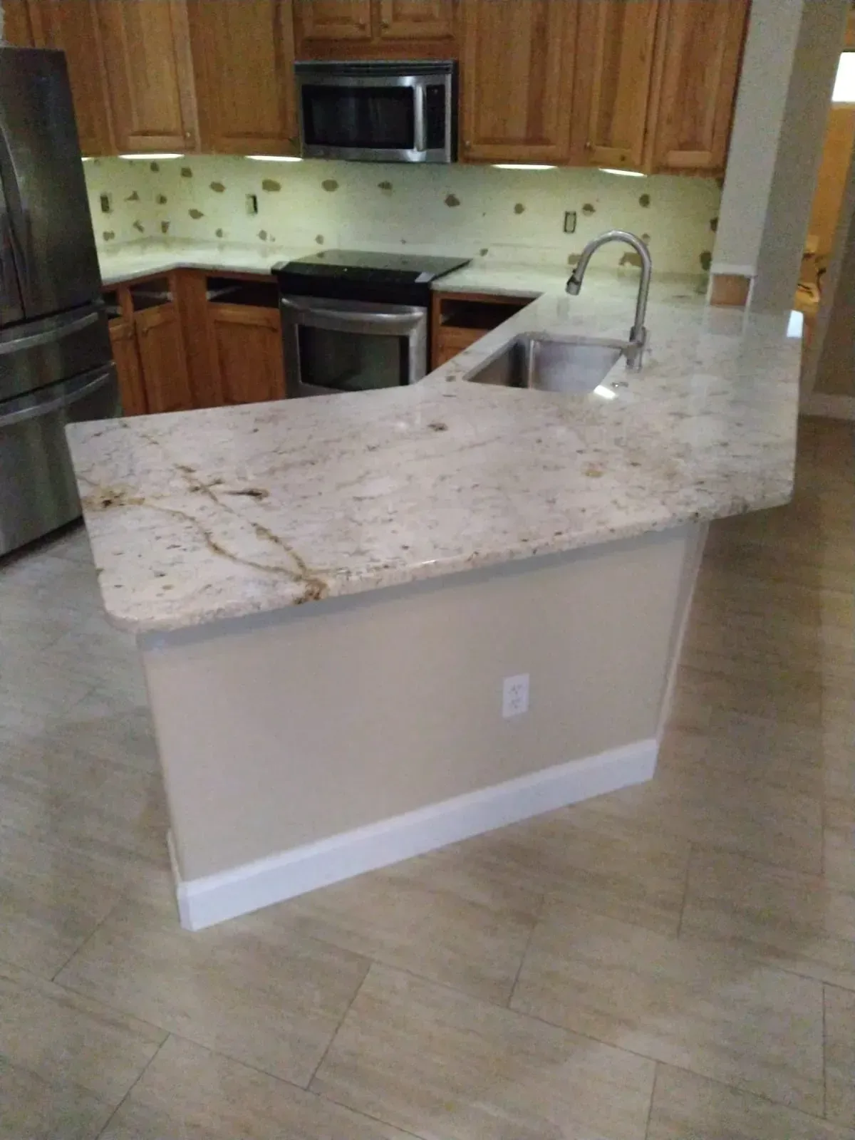 Kitchen with granite island countertop, sink, and wooden cabinets, viewed from the dining area