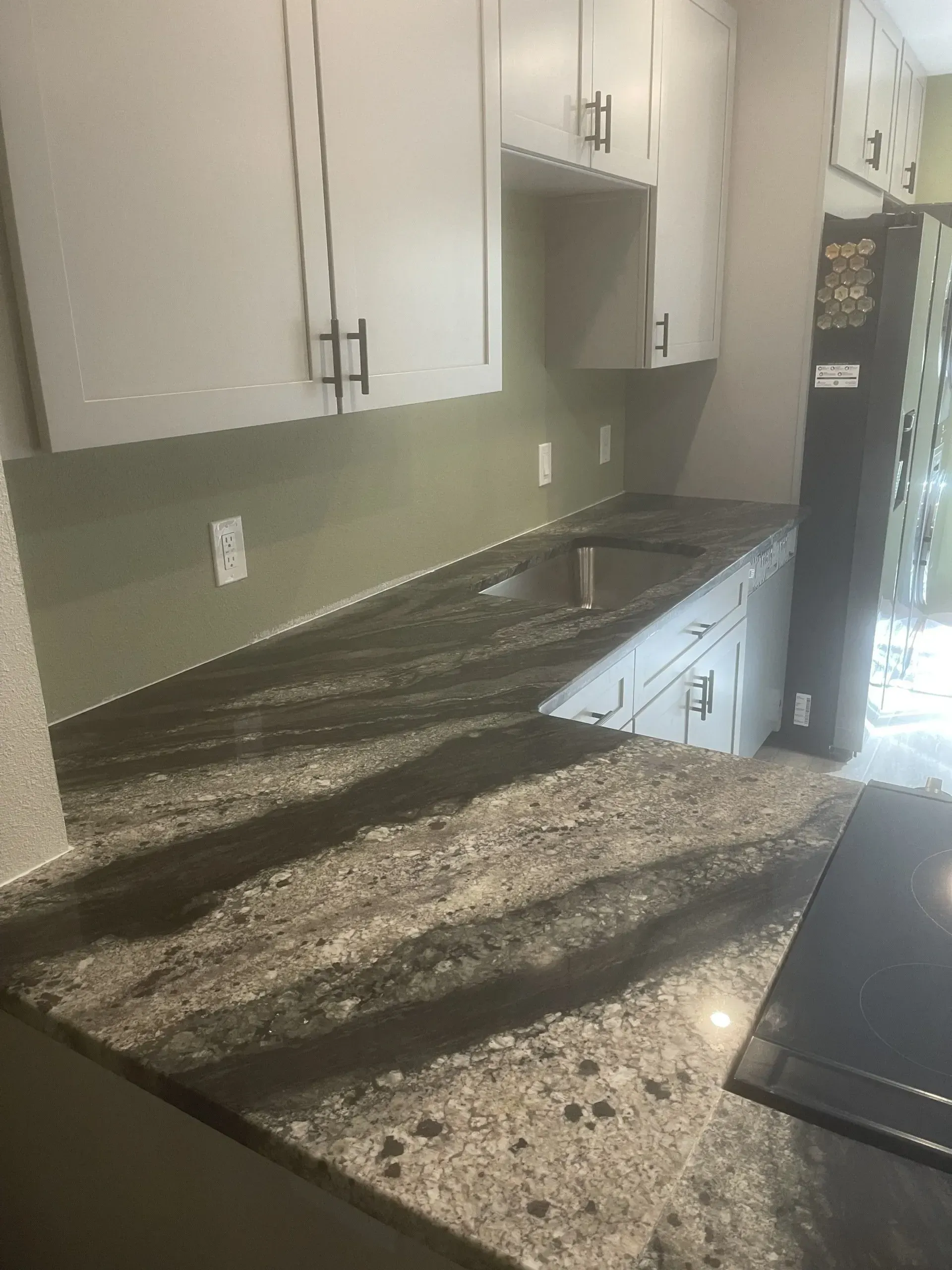 Empty kitchen with granite countertops, white cabinets, and a black refrigerator.