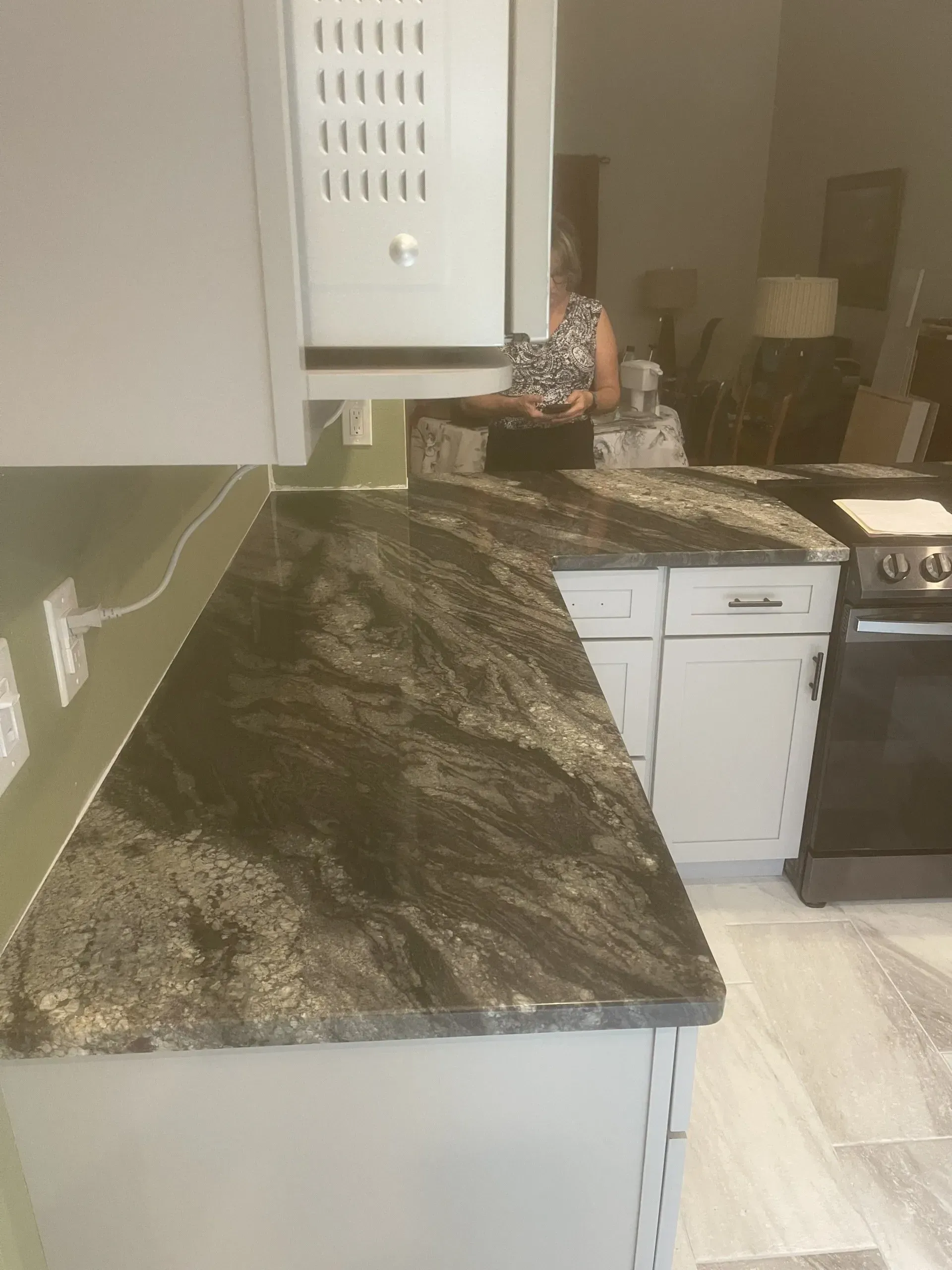 Kitchen countertop with dark granite, white cabinets, and a person seated at a table in the background.