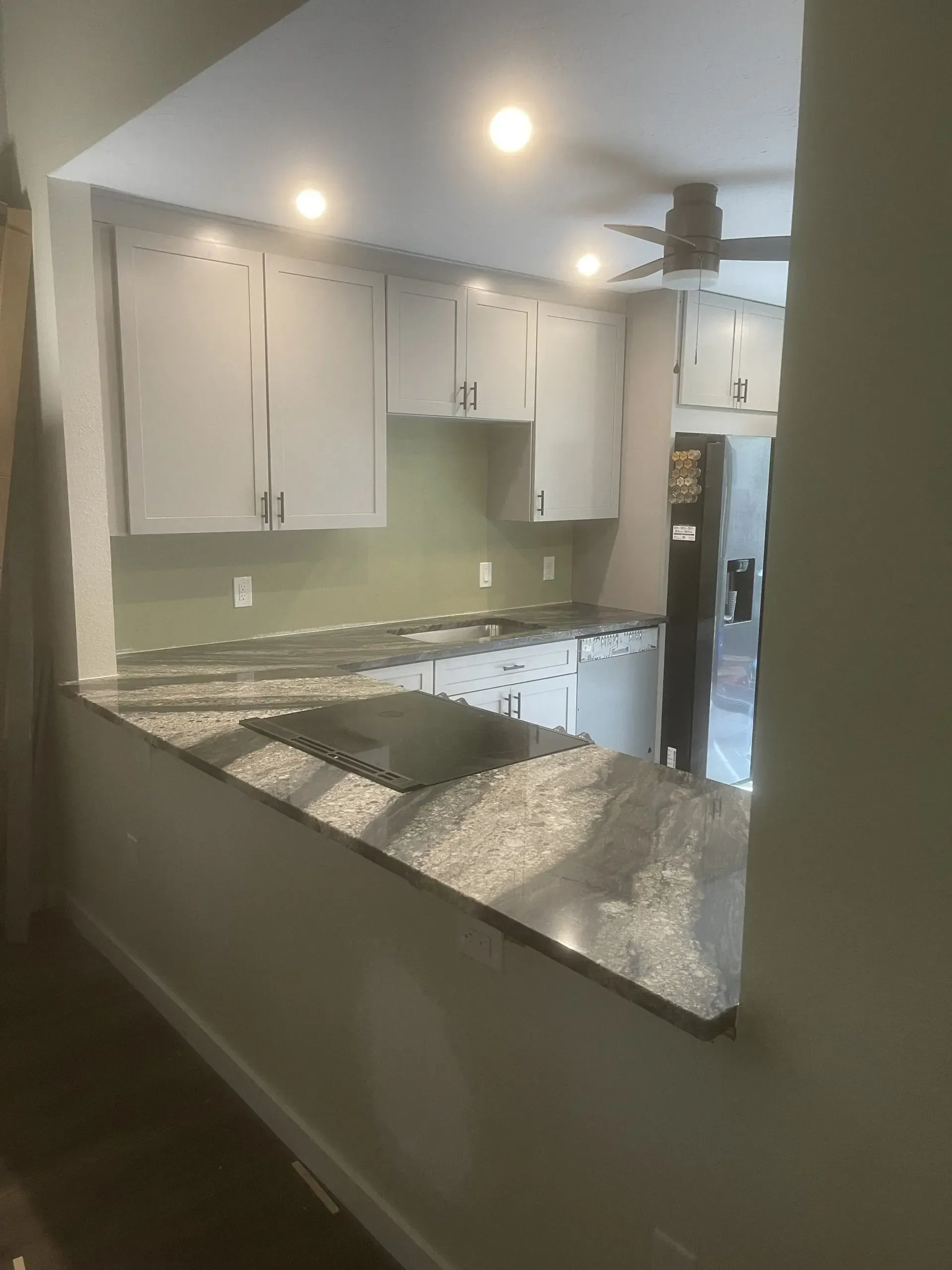 Modern kitchen with white cabinets, granite countertops, green walls, and recessed lighting
